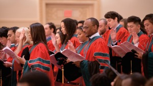 Students, wearing their red gowns, recite the Hippocratic Oath, as they stand holding a booklet in their left hand with their right hand raised